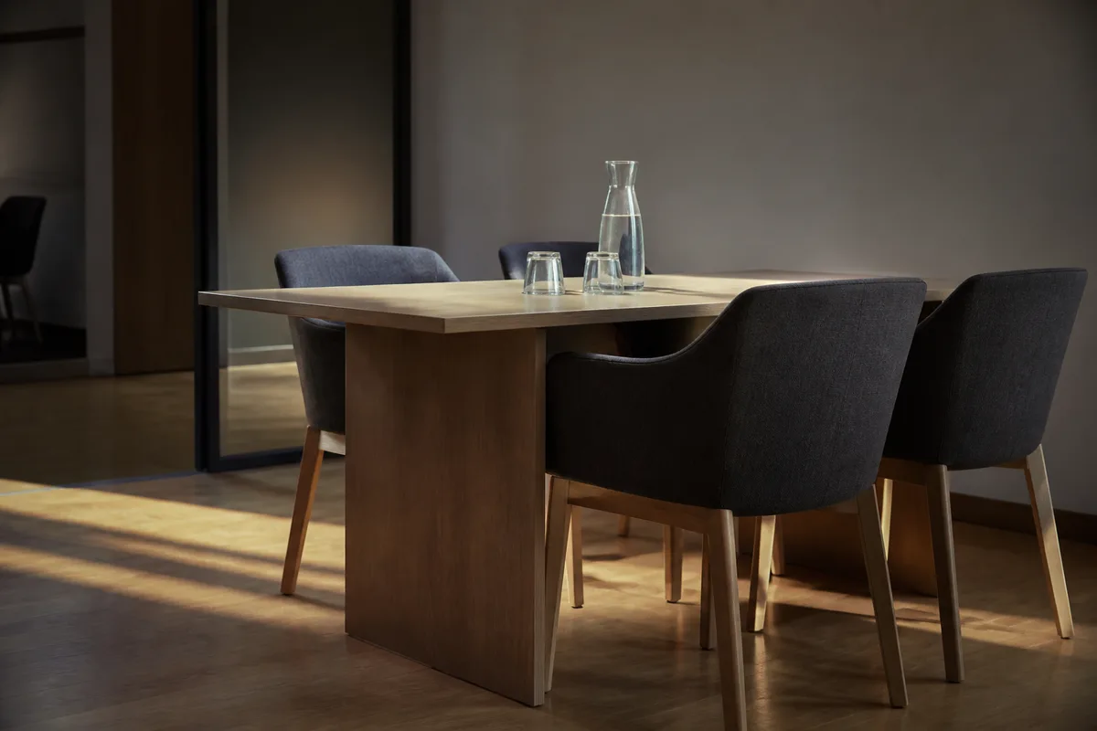Salle de réunion vide baignée de lumière naturelle, chaises alignées autour d’une longue table en bois clair